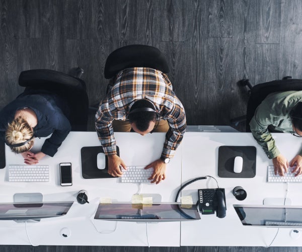 Aerial view from above of three people typing on white keyboards