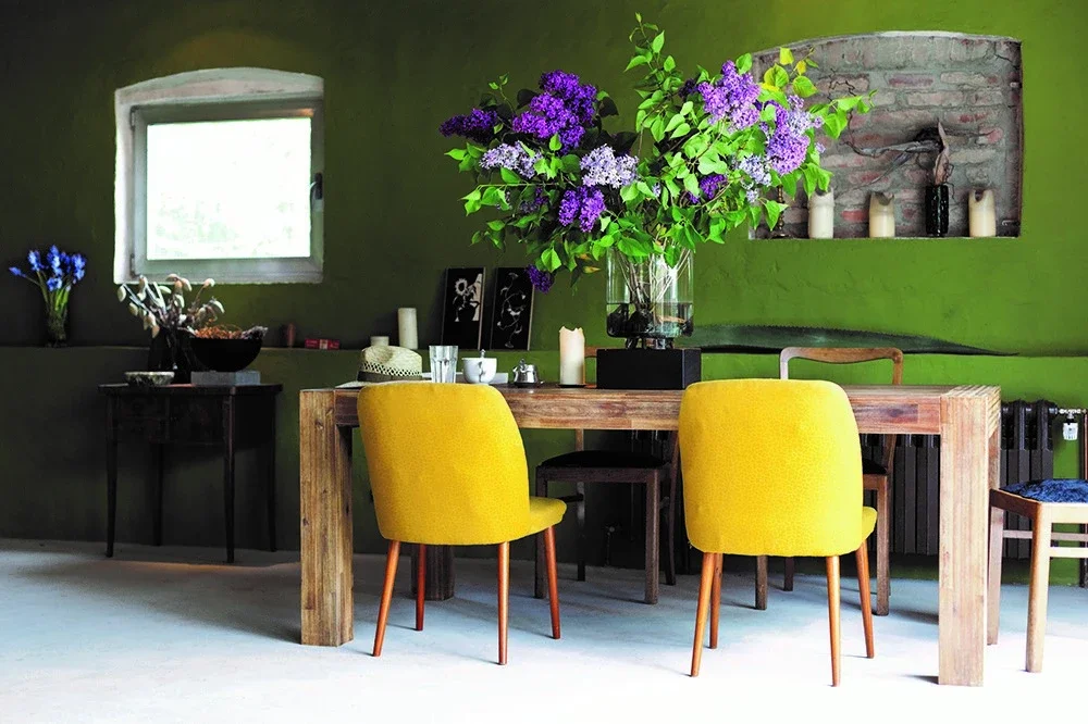 Una mesa con sillas amarillas y un jarrón con flores moradas
