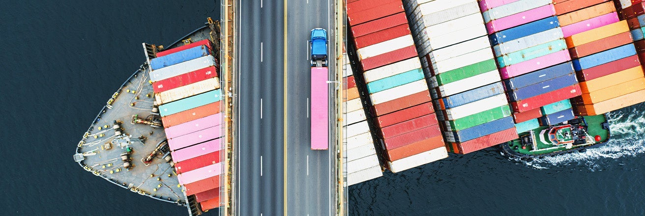 A truck on the bridge with a ship underneath