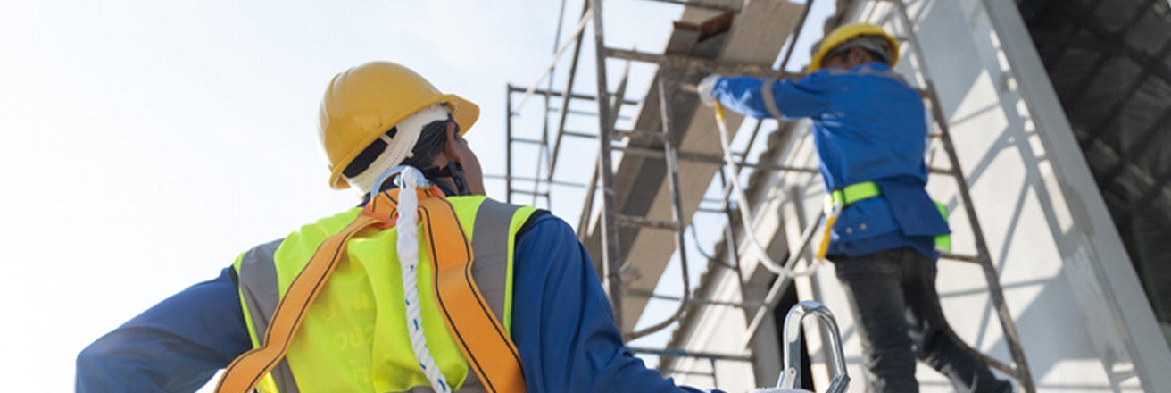 Two men wearing hard hats and PPE on scaffolding working on the side of a building
