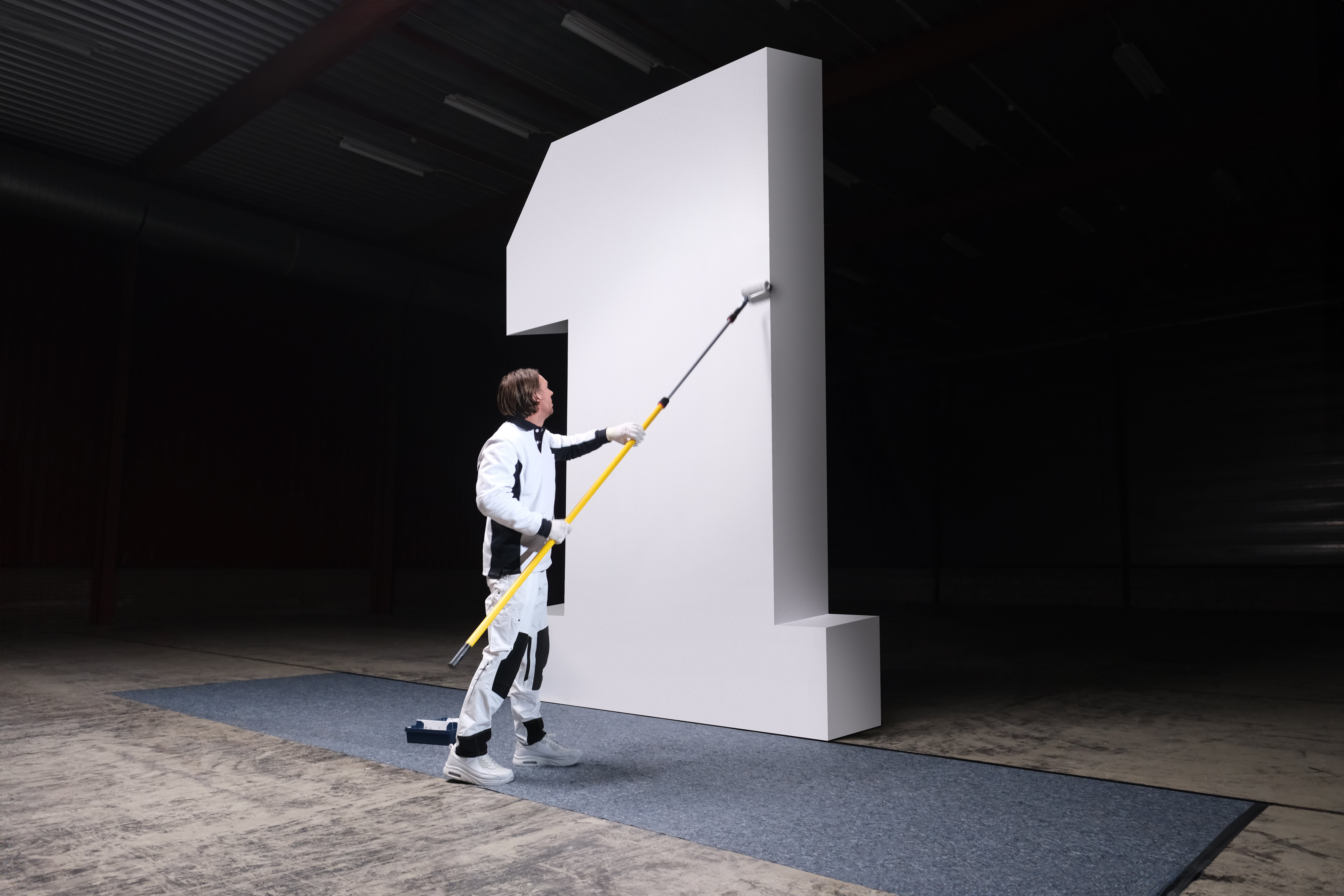 A man in a white suit painting a large white wall