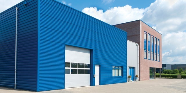 Modern industrial warehouse with blue cladding and attached office under clear blue sky