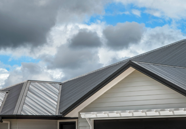 Black meal roof of a house with cloudy sky.