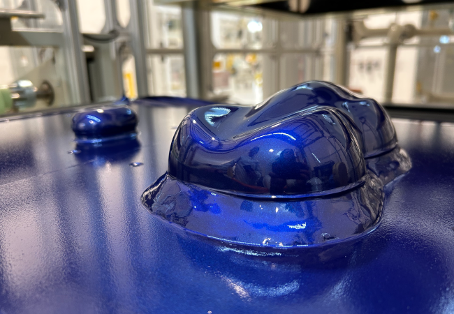 Close-up of glossy blue vacuum-thermoformed material shaped into raised automotive component forms on a factory surface.
