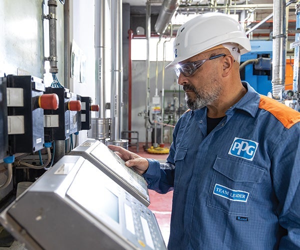 Male PPG worker in PPE using equipment within manufacturing plant