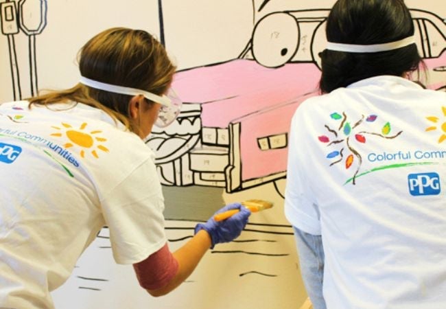 Two women painting mural of funny animated pink car