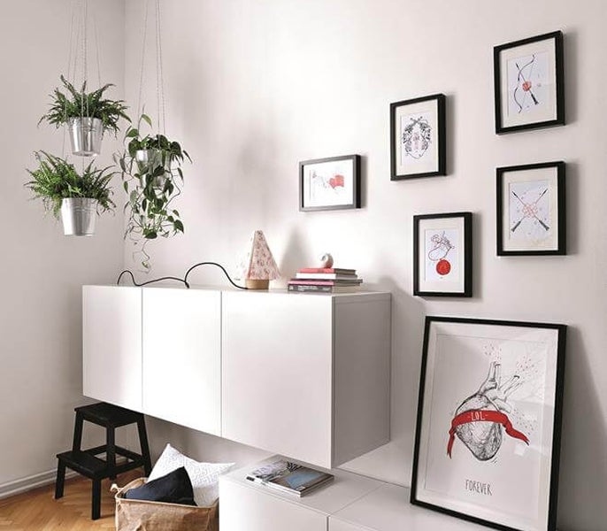 A white cabinet with pictures and a plant on the wall