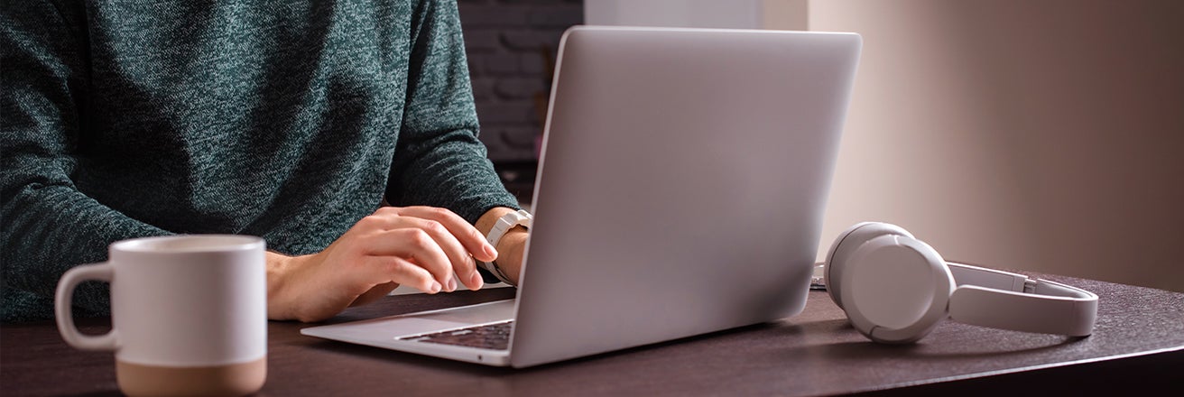 Woman sat at a table wearing a green jumper typing on a laptop with headphones coated using grey excimer technologies