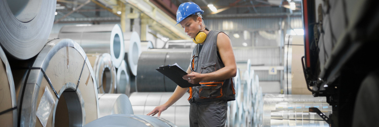 Man with a blue hard hat and yellow headphones looking at rolled steel