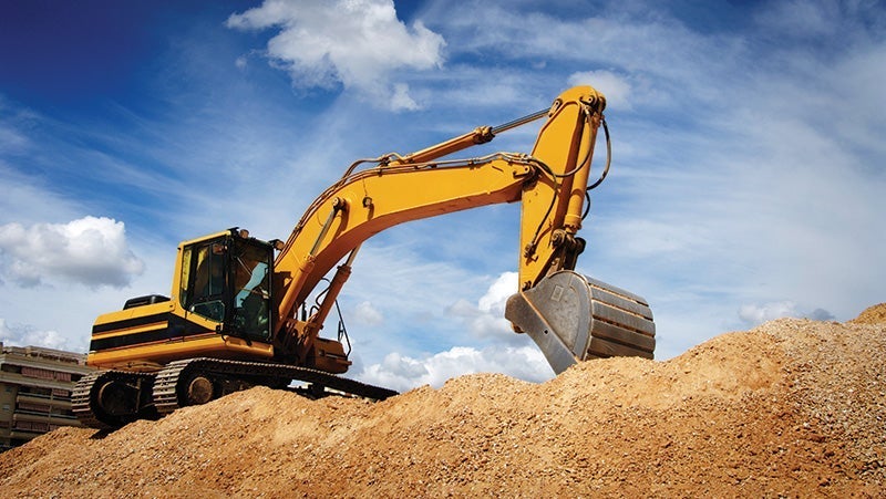 Yellow excavator moving dirt on a construction site under a blue sky with clouds