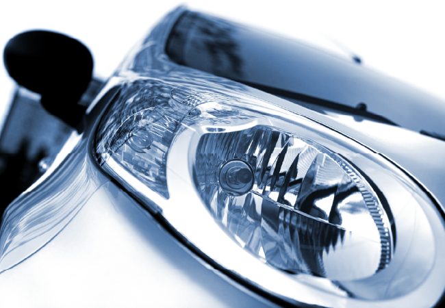 Detailed close-up of a car headlight showing the clear lens, internal reflectors, and smooth painted body panel.