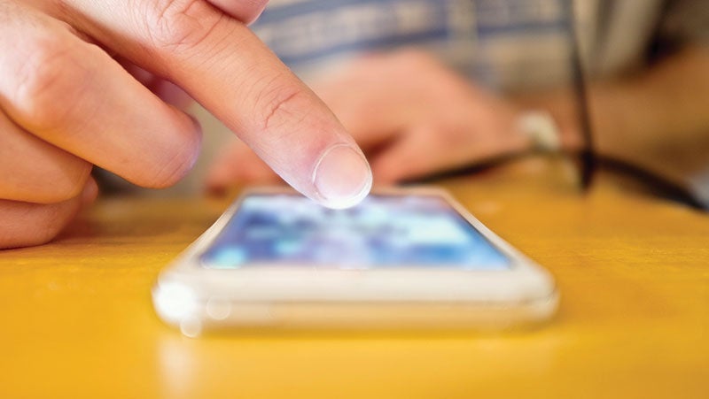 Close-up of a person's finger touching a smartphone screen on a wooden table