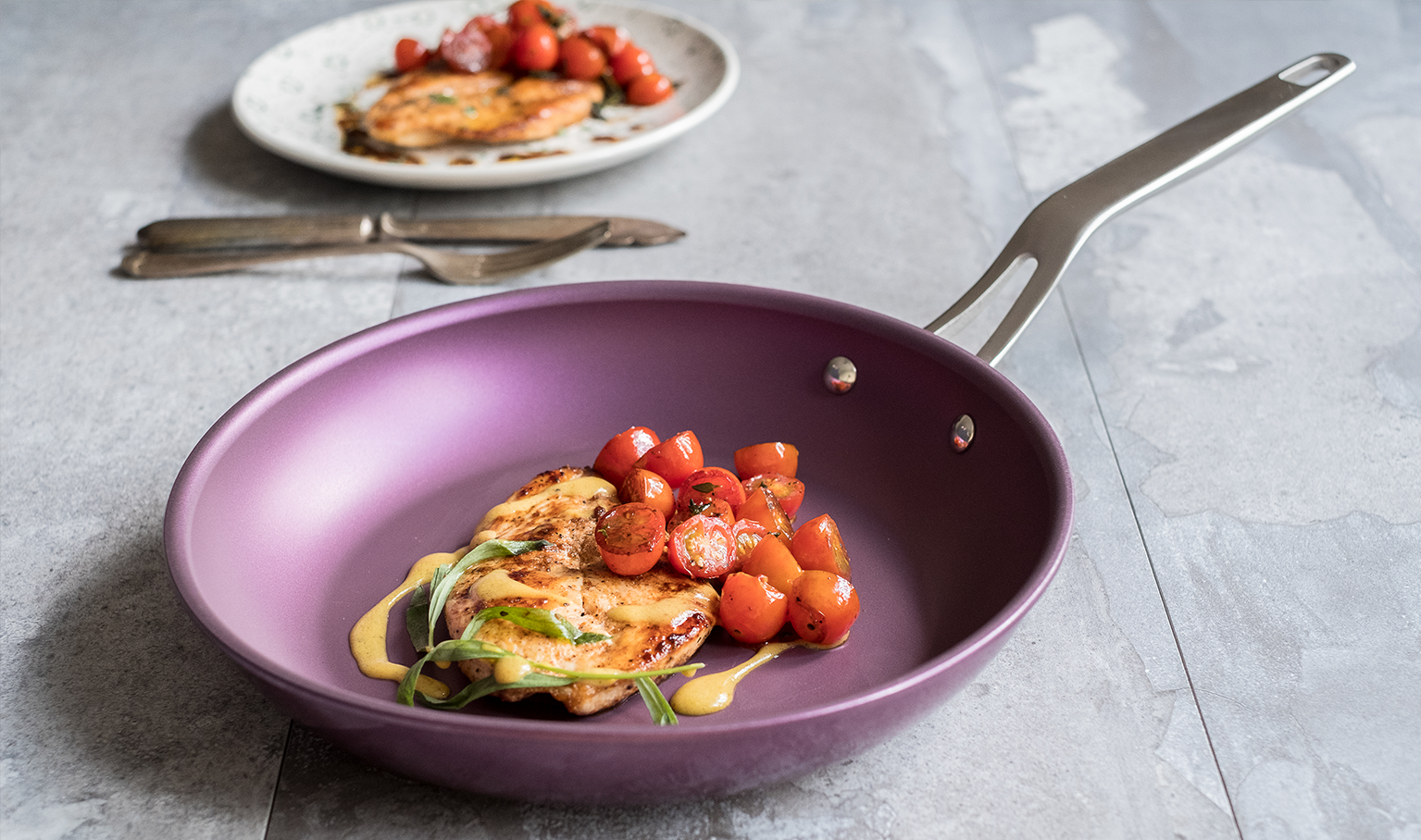 Purple Eterna coated pan with chicken and cherry tomatoes on a grey kitchen surface