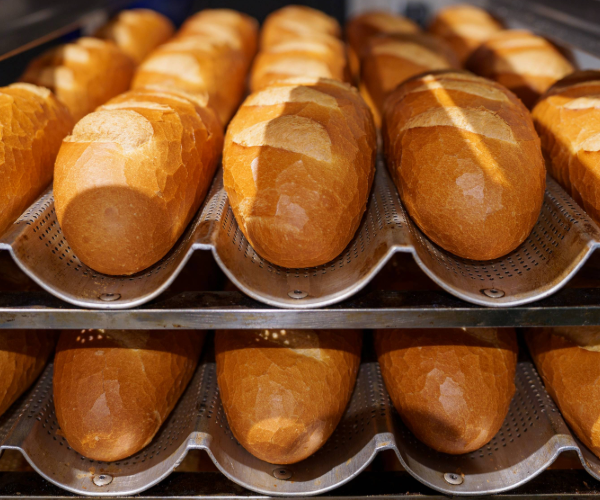 Front view of silver bread trays with perforated base holding several baked rolls