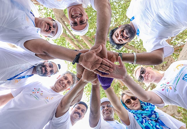 Group of volunteers as part of PPG's Colorful Communities in a circle with hands in middle