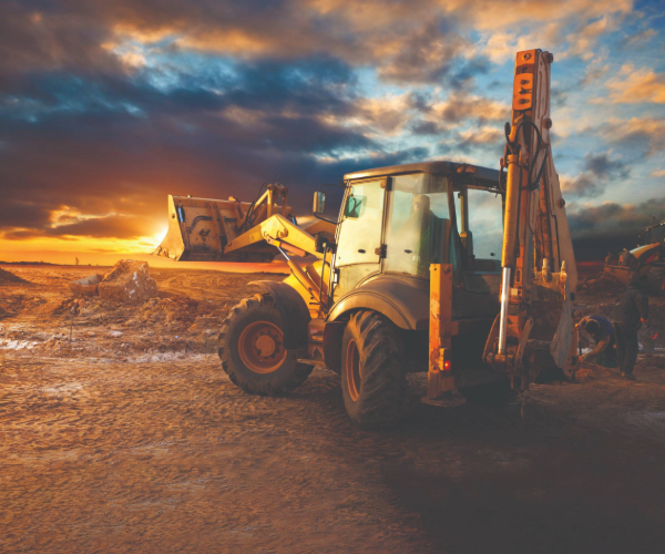 Construction Excavator with raised bucket facing a sunset sky