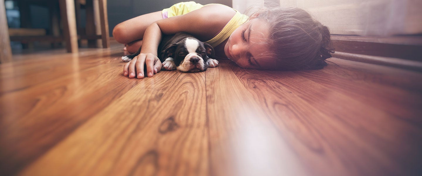 Young child in a yellow shirt resting on a hardwood floor with a sleepy puppy, conveying a peaceful and comforting moment.