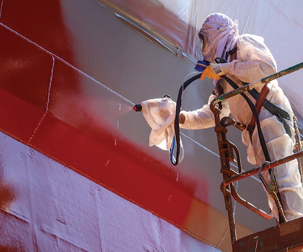 Worker wearing PPE spraying ship with red coating