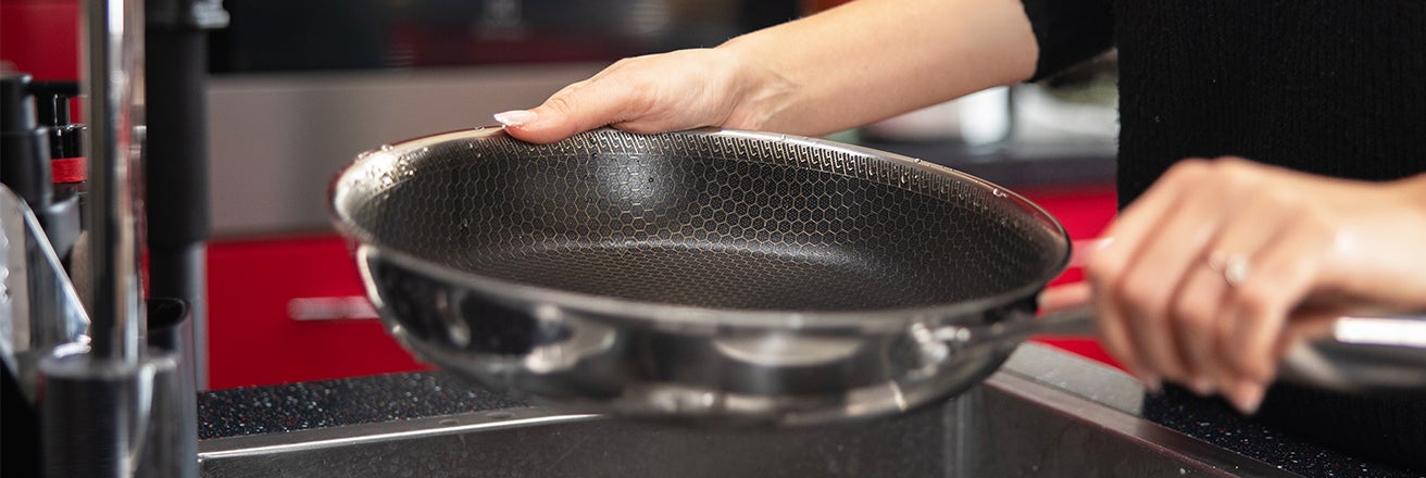 Pan coated with Fusion Edge black solgel ceramic coating being held by a woman in a kitchen environment with red and black background