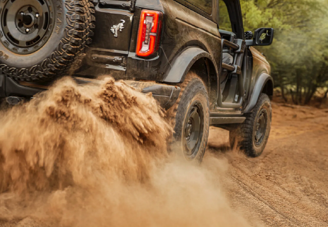 Rear view of an off-road SUV driving on a dirt trail, kicking up dust and sand from the tires.