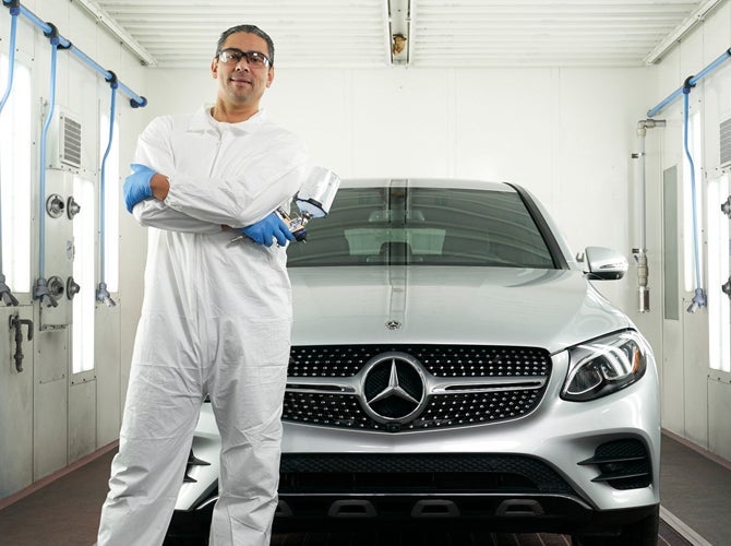 Employee with spray gun standing next to car in spray booth