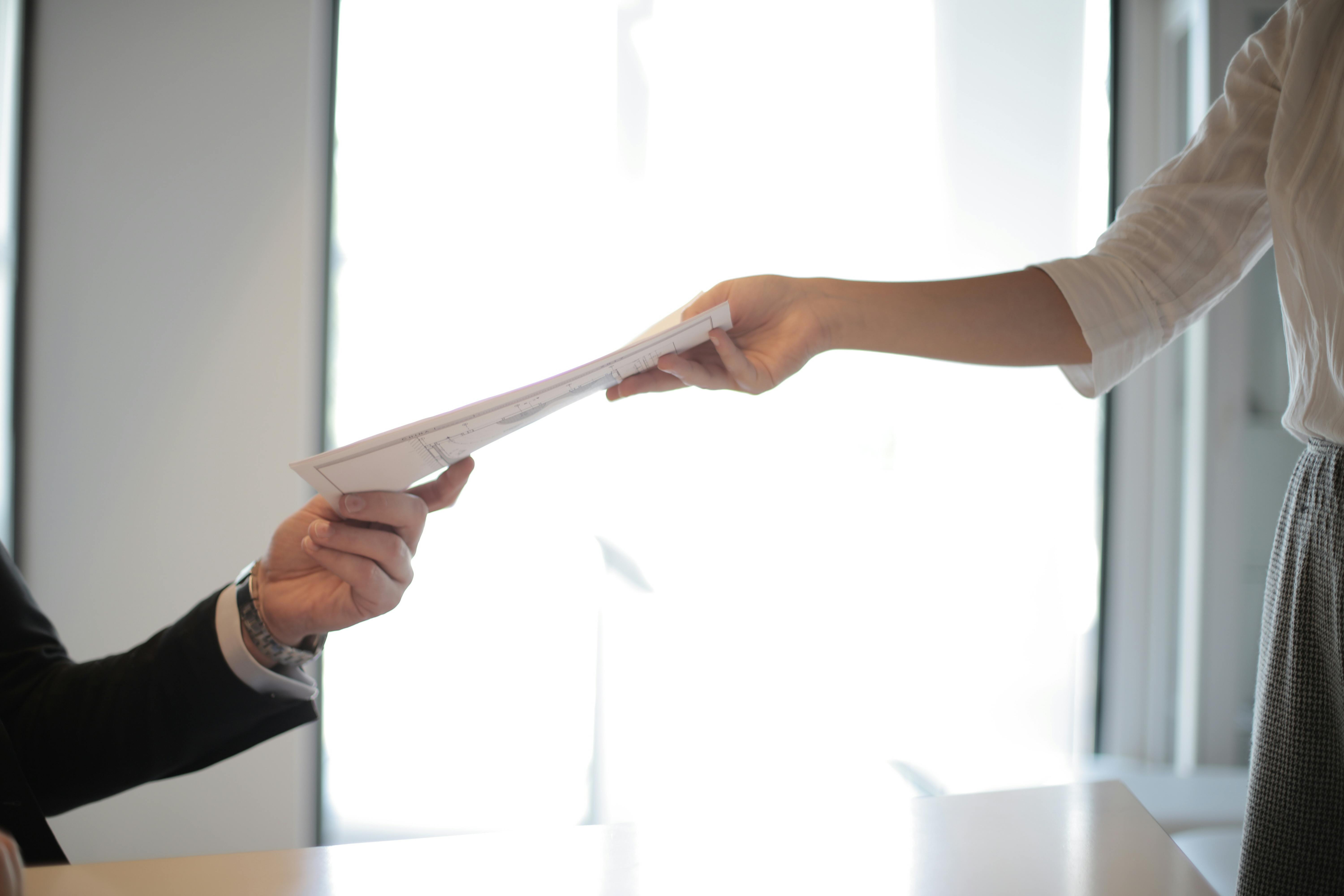 Two office workers wearing business dress passing paperwork between them