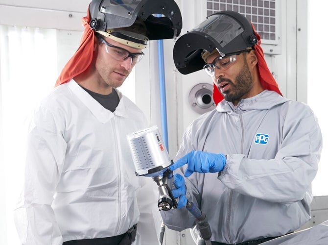 Two male PPG employees wearing PPE discussing details of spray gun