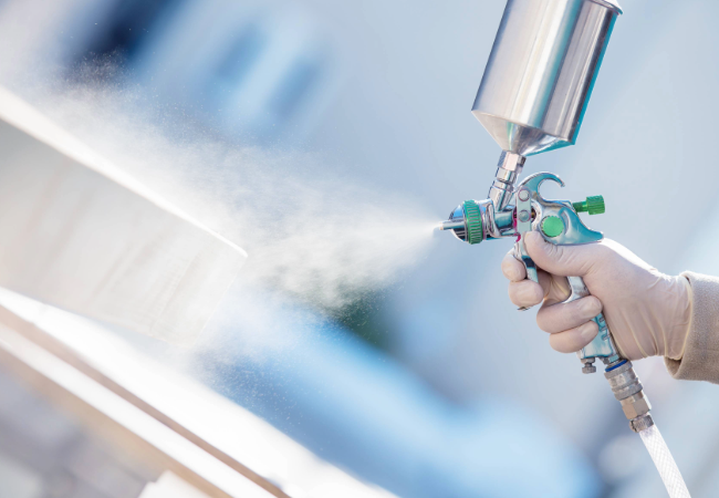 Gloved hand spraying liquid coatings from a silver and green spray can