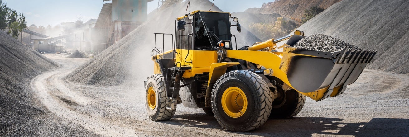 Yellow and black bulldozer carrying a full load of gravel through a dusty quarry