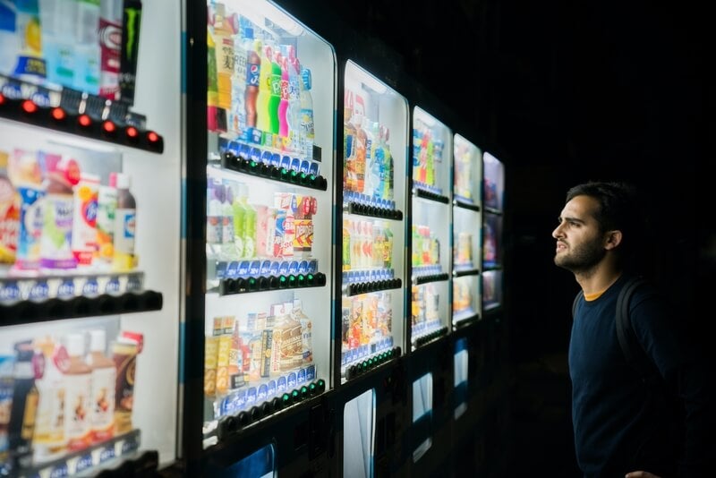 Photo by Victoriano Izquierdo on Unsplash, a bearded man looking at refrigerated drinks