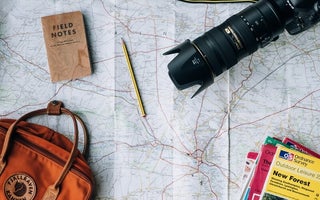 Photo by Annie Spratt on Unsplash, which shows a map laid out with a large camera, hand bag and the books on top with a pencil