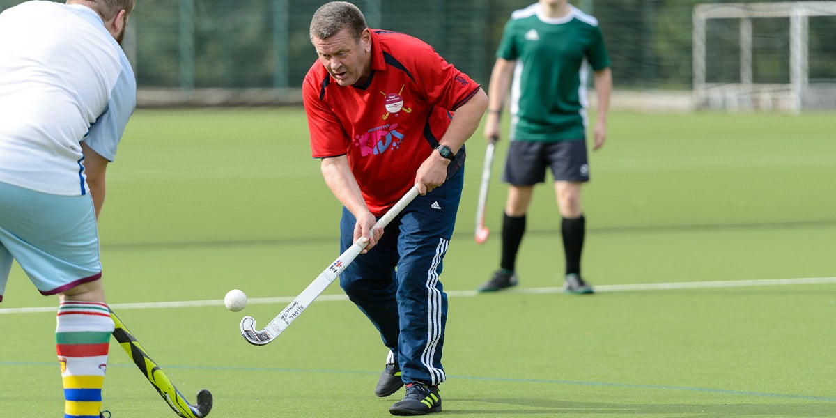 Adult male playing hockey on a green pitch 