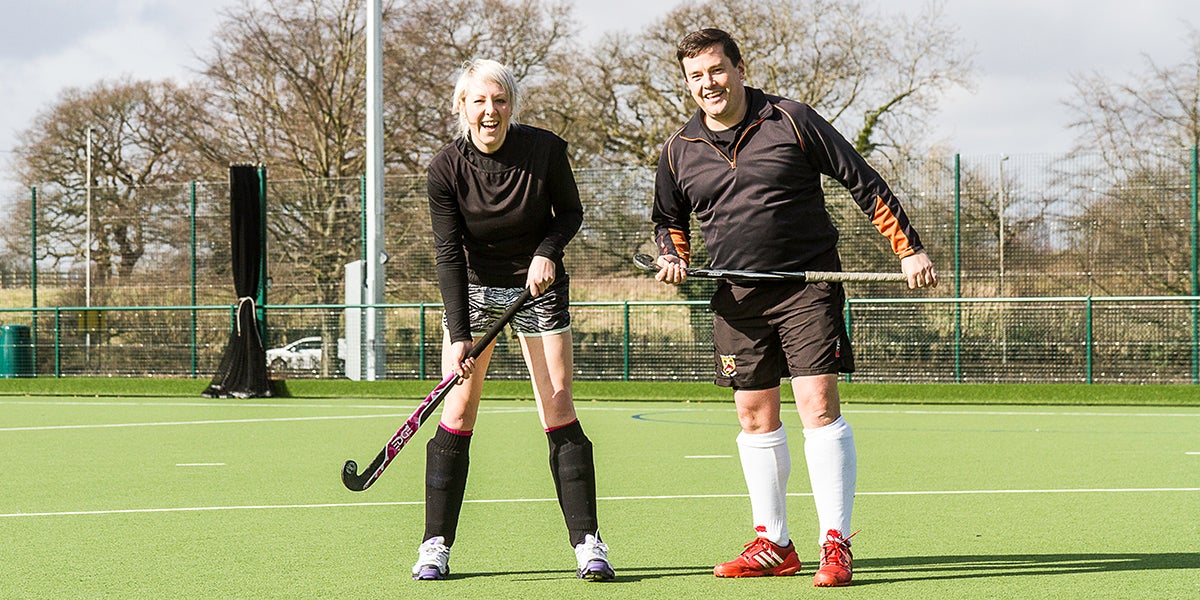 Male and female playing hockey on a green pitch 