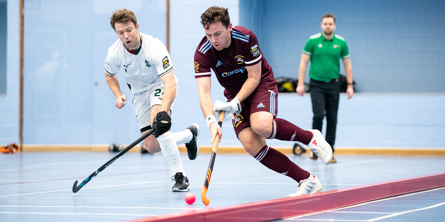 Male Indoor Hockey player running with ball and another player chasing 