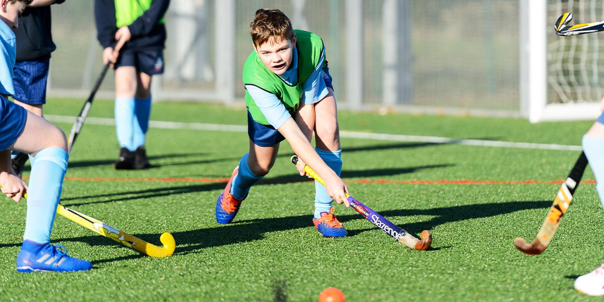 Young boy playing hockey on a green pitch 