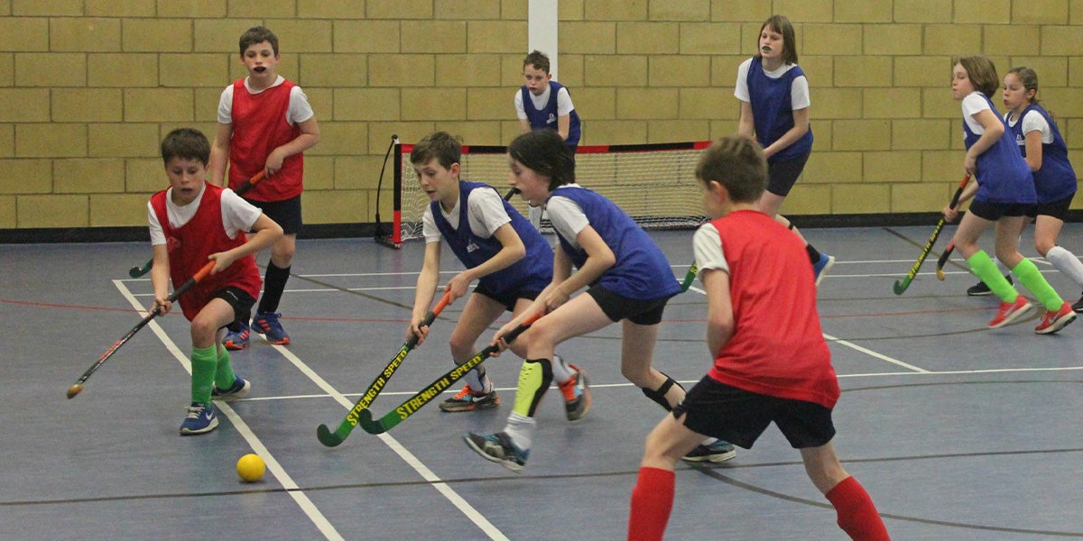 School children playing hockey in a sports hall