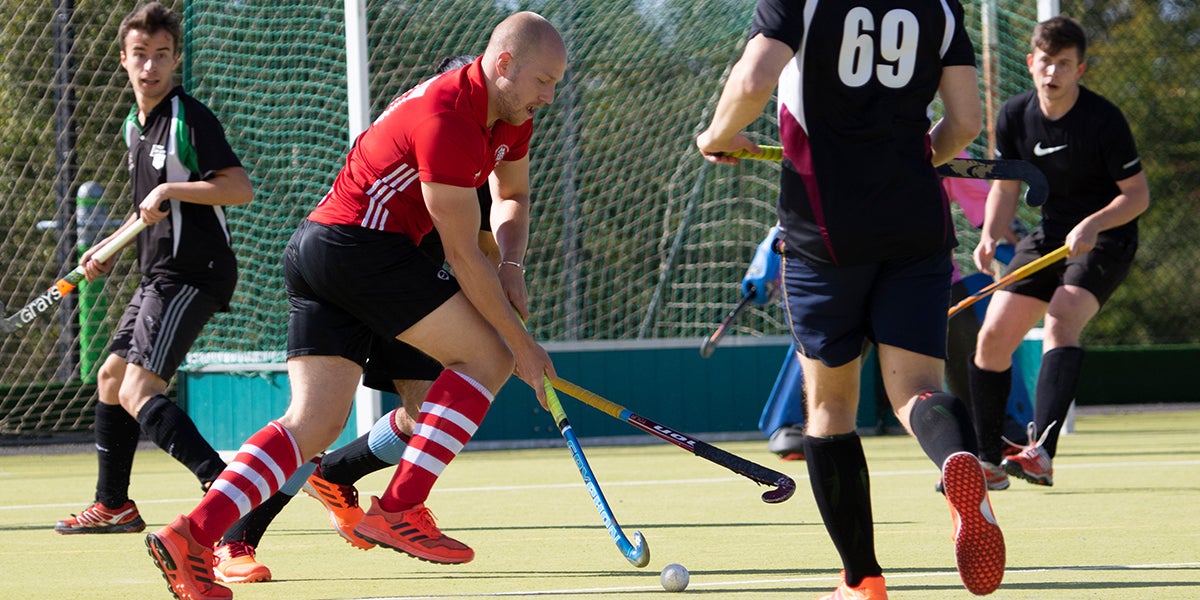 Male hockey players playing on a green pitch 