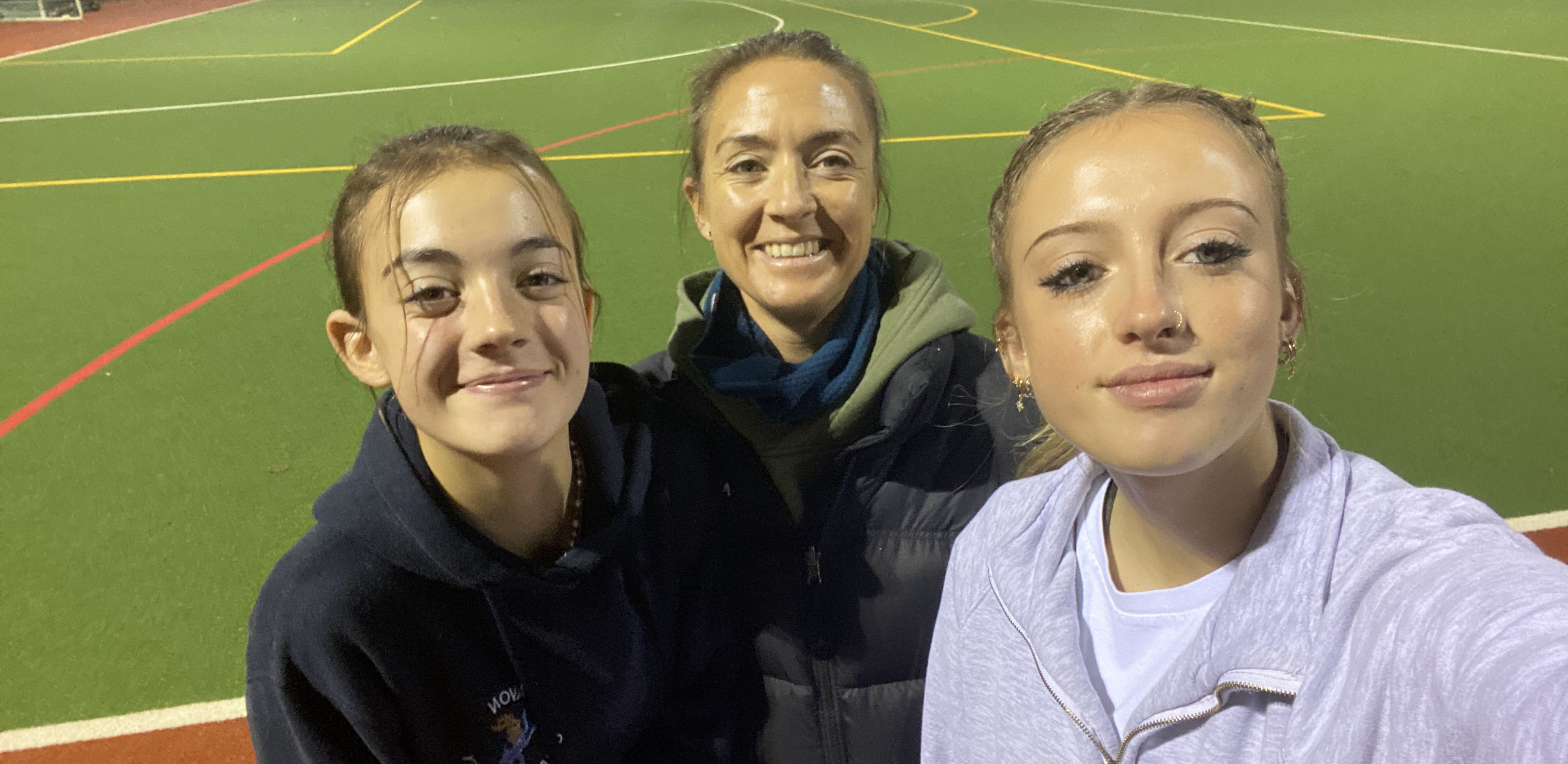 A mother with her two daughters by a hockey pitch
