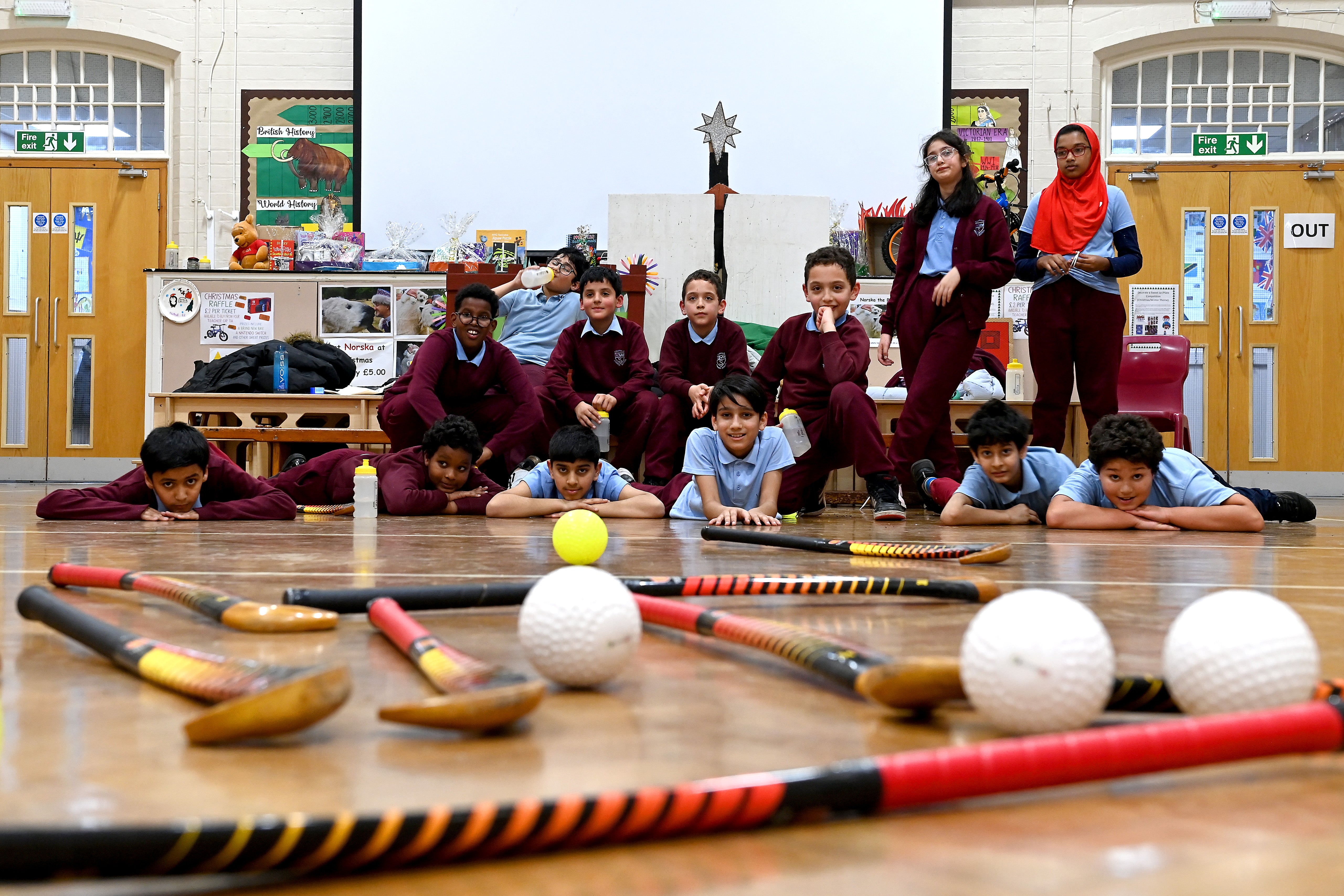 School children in a hall with hockey sticks and balls