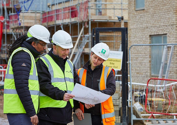Three people wearing high visibility jackets looking at a development plan on a building site.