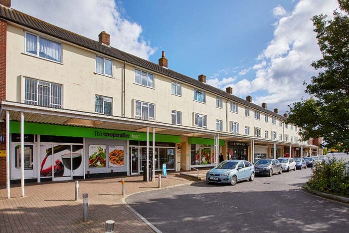 A picture of some shops, with cars parked out in front.