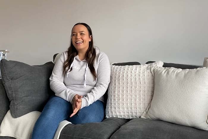 Olivia smiling and sitting on her sofa at home