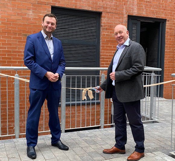 Two men standing in front of a new development about to cut a ribbon to celebrate the opening of new homes.