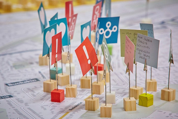 A area map laid on a table, which has small blocks with flags on them. The image is akin to a strategy map used in warfare to plot places on the map.