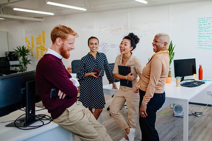 A group of people in an office setting, standing around some desks.