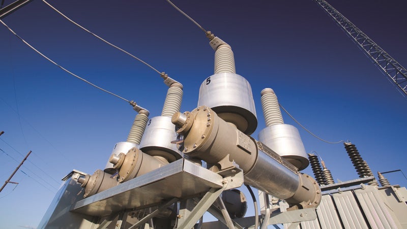 Three large high voltage power transformers with attached bushings under a clear blue sky, showcasing industrial electrical equipment for power distribution