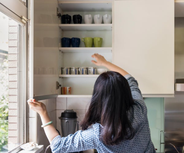 Woman with dark hair reaching into a kitchen cupboard to get a mug