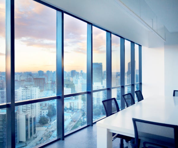 Office environment showing a meeting table and chairs with large windows over-looking a city with tall buildings