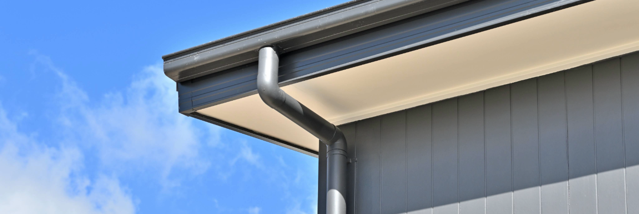 Roof close up with drain pipe and guttering set against a blue sky