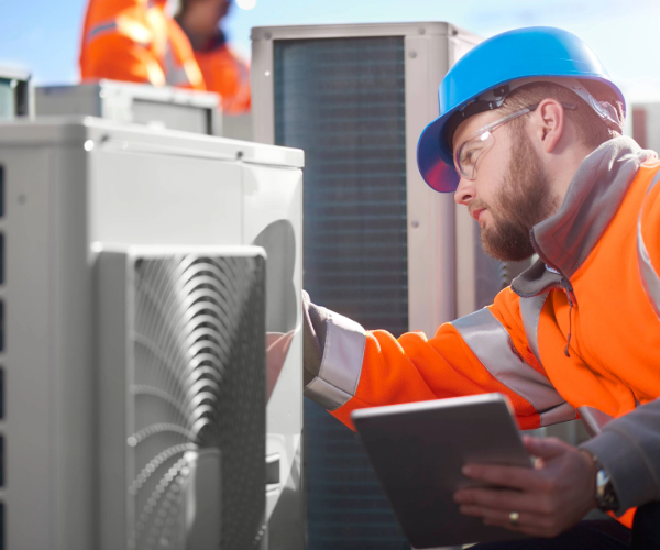 Man in a blue hard hat and orange workwear inspecting an air ventilation system